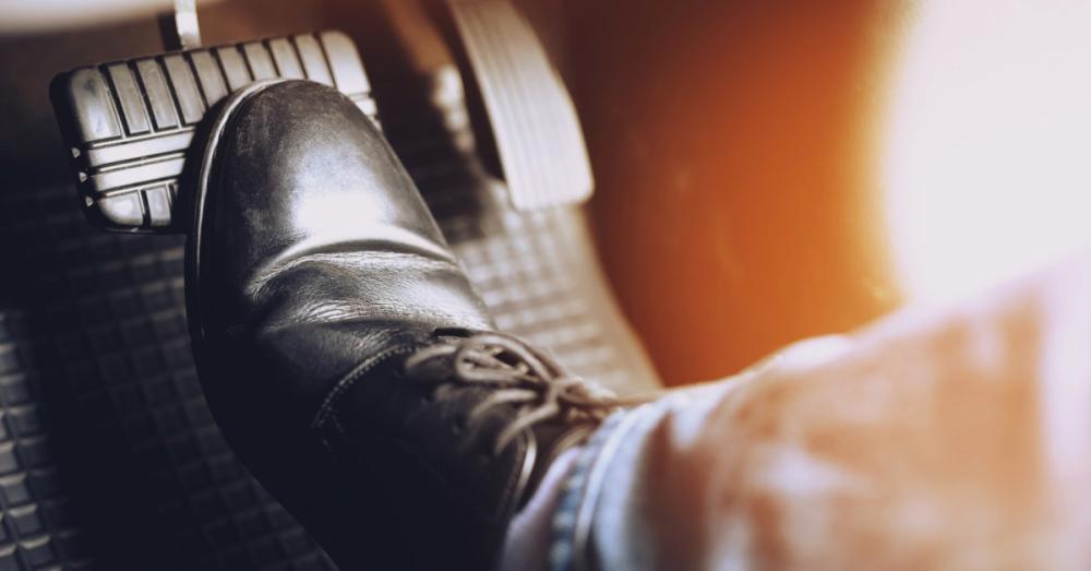 A person with a black shoe pressing down on their car's brake pedal. The person is wearing a black shoes and jeans.