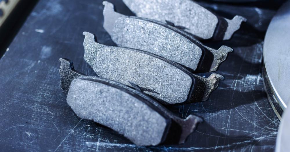 Semi-Metallic vs. Ceramic Brake Pads: Pros and Cons A close-up of four automotive brake pads on a metal workbench beside a brake rotor, showing textured friction surfaces.