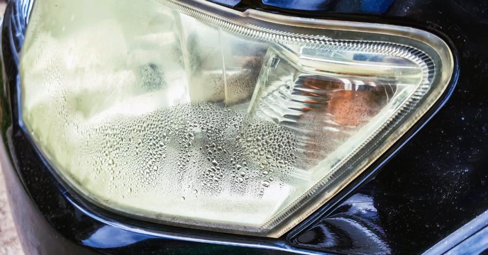 Causes of Fogged Headlights and How To Repair Them A heavily fogged headlight lens on a black car with moisture and water droplets condensed on the inside of the lens.