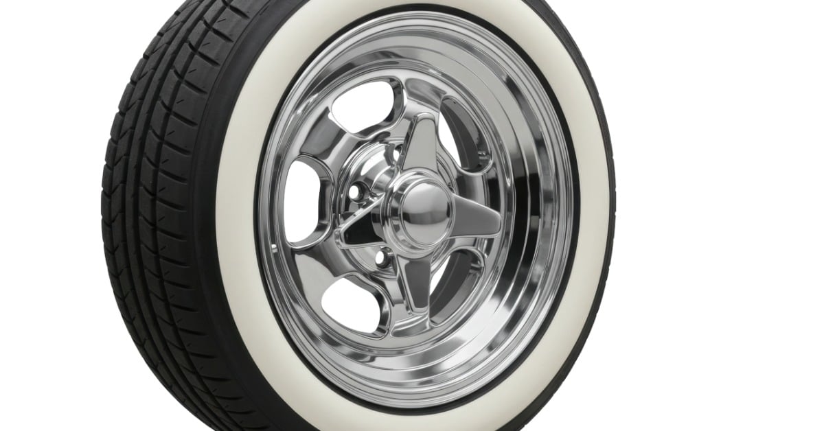 A white wall tire stands at an angle with black tread around the outer edge. It has a shining, silver-colored wheel.