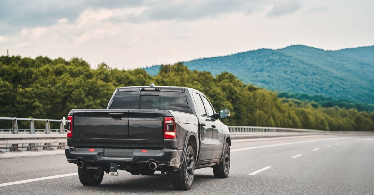 Semi-Metallic vs. Ceramic Brake Pads: Pros and Cons A black pickup truck drives on a highway with lush green trees and rolling mountains in the background.