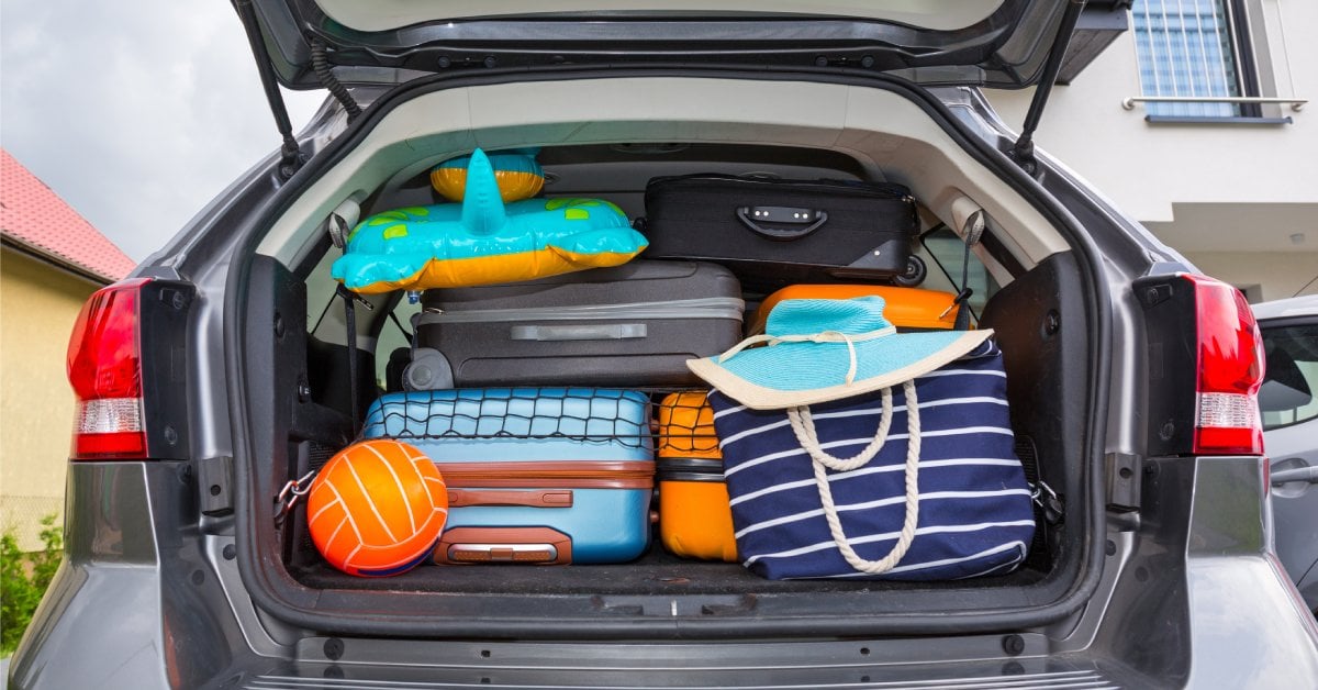 A car with an open trunk that's packed with suitcases and items for the beach. The trunk looks overpacked.