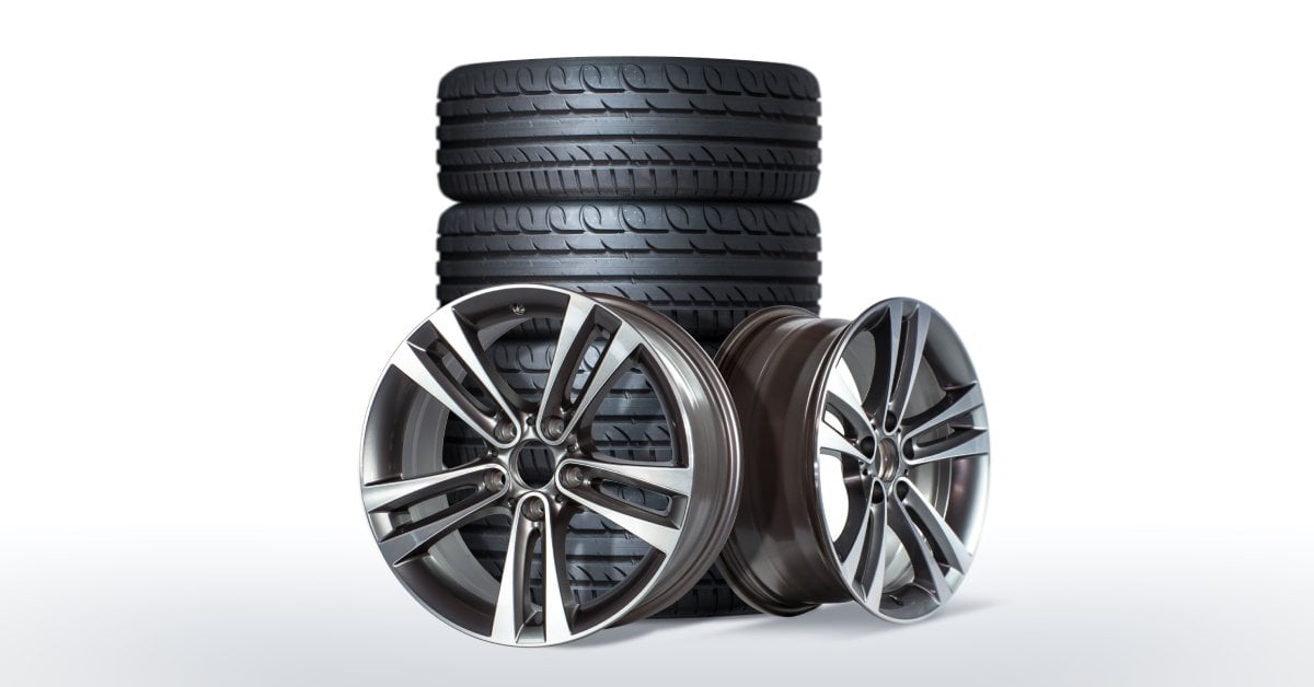 A set of two car rims and four tires. The tires are stacked together, with the rims sitting up against them.