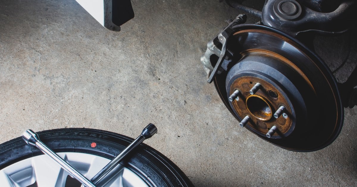 An exposed wheel mount with a wheel lying on the ground next to it. The wheel has a tire iron laying on top of it.