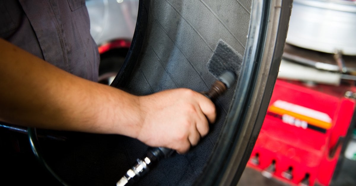 A car mechanic using a tool to patch the inside of a tire. The tire is currently removed from the rest of the wheel.