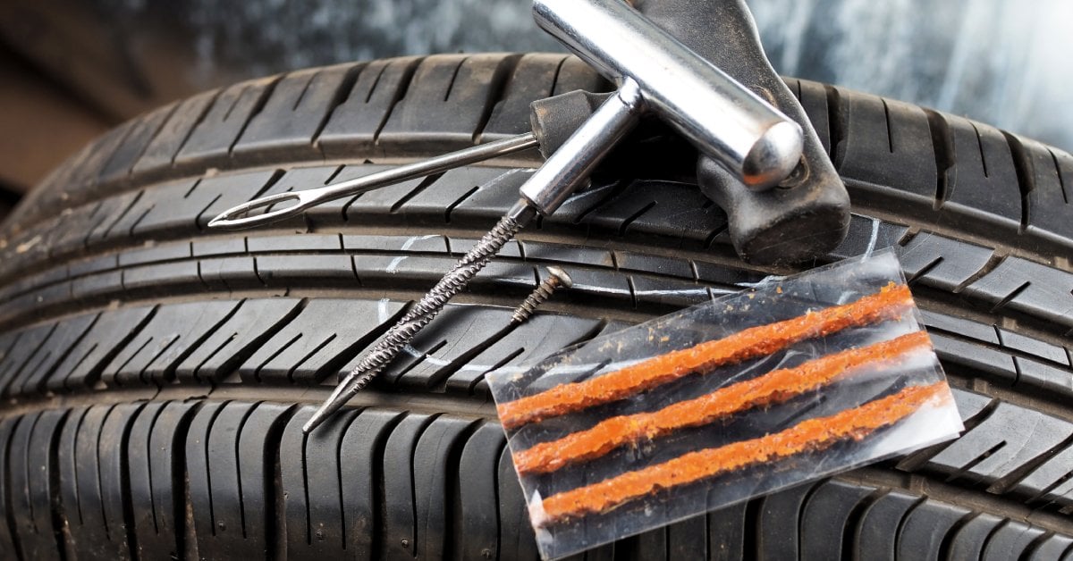 The top of a tire with a tire repair kit sitting on top of it. The kit has the all tools and plugging equipment needed.