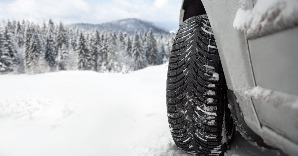 The front edge of a vehicle with the tire turned all the way to the right. The tire has some snow stuck in its treads.