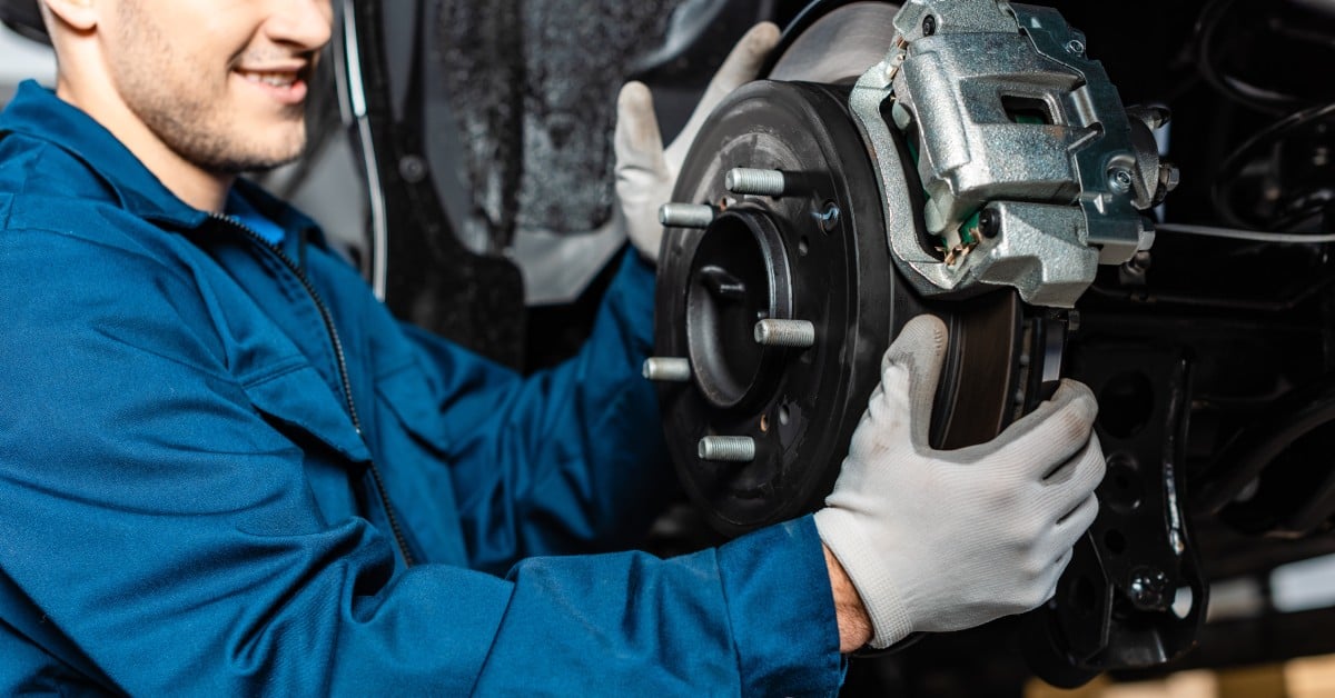 An automotive mechanic stands next to a wheel housing as he tries to change the disc brakes on the car.
