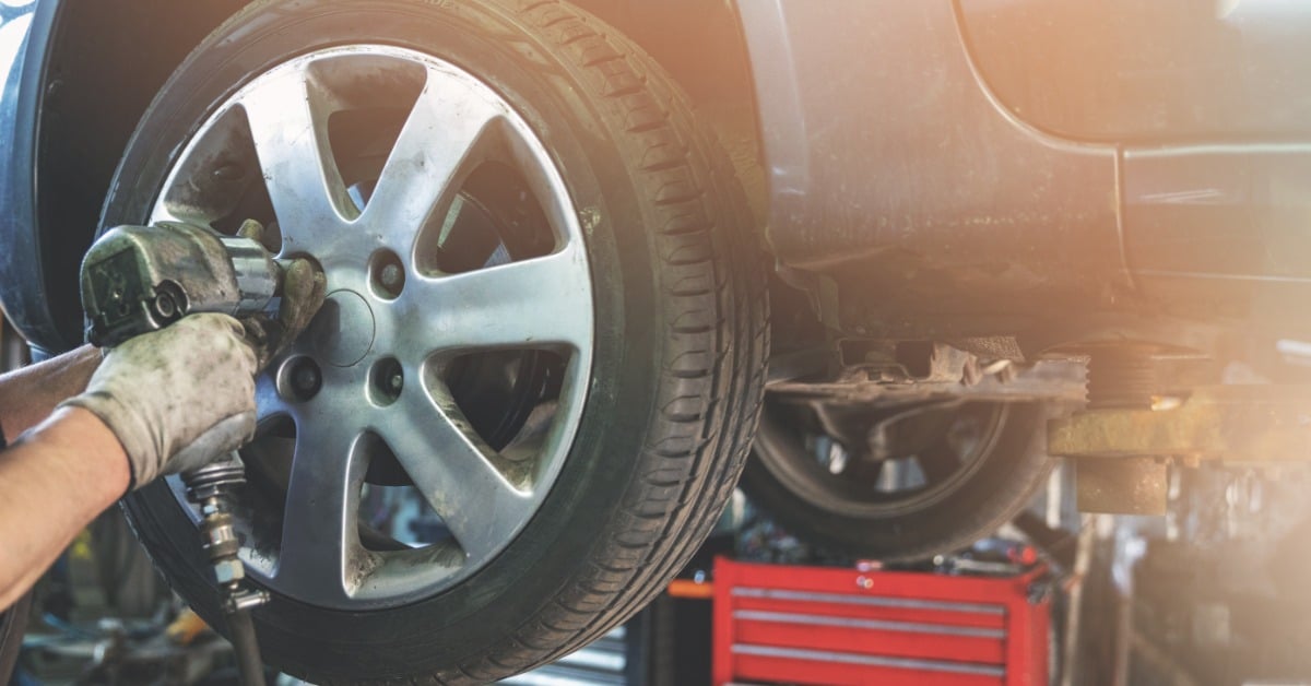 A mechanic uses a power tool to remove a car wheel during a tire rotation service at an auto repair shop.