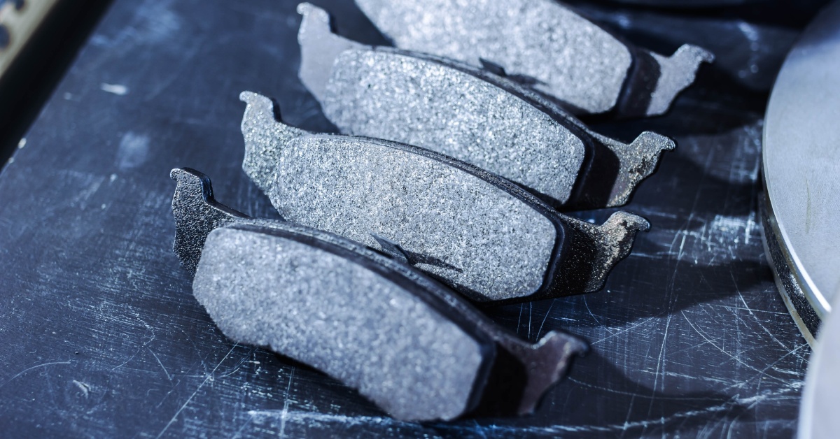 A set of worn brake pads displayed on a dark scratched surface, showing friction material and metal backing plates.
