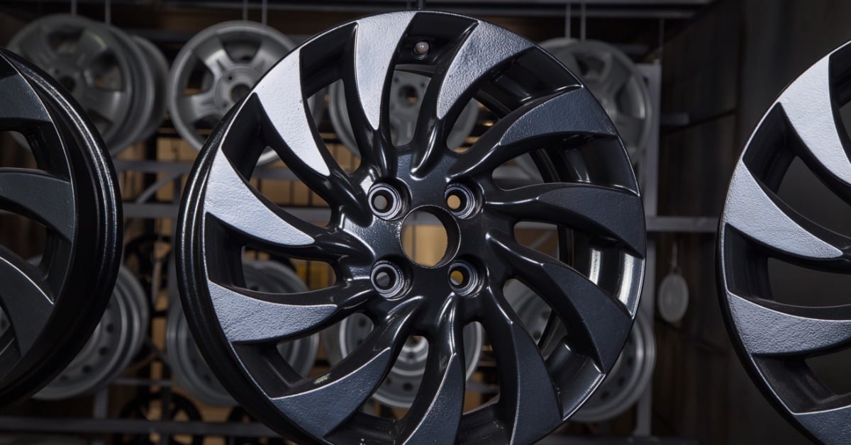 An automotive shop displays a black powder-coated wheel on a rack, highlighting its finished protective coating.