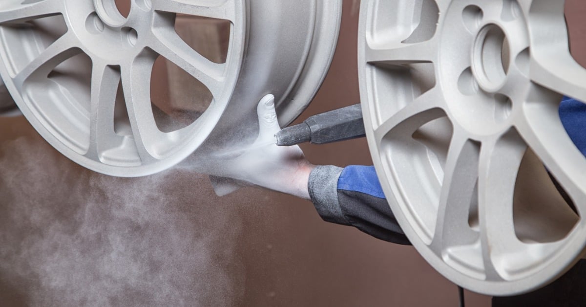A person applies powder coating to vehicle wheels in a workshop, demonstrating a protective finishing process.