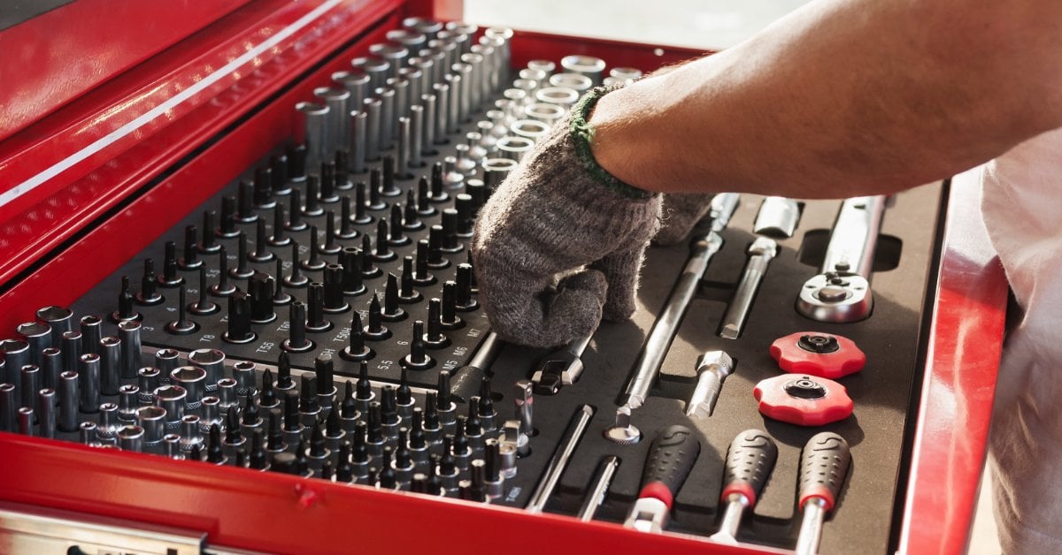 How To Replace Your Car’s Headlight Assembly A person wearing gloves looks through an organized red toolbox filled with wrenches, ratchets, and automotive repair tools.