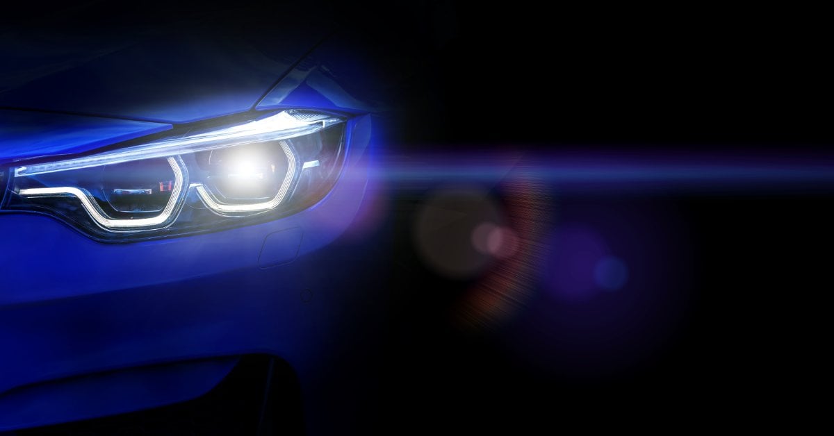 How To Replace Your Car’s Headlight Assembly A close-up of a blue car's headlights shining brightly in the dark, showing LED lighting details and lens flare.