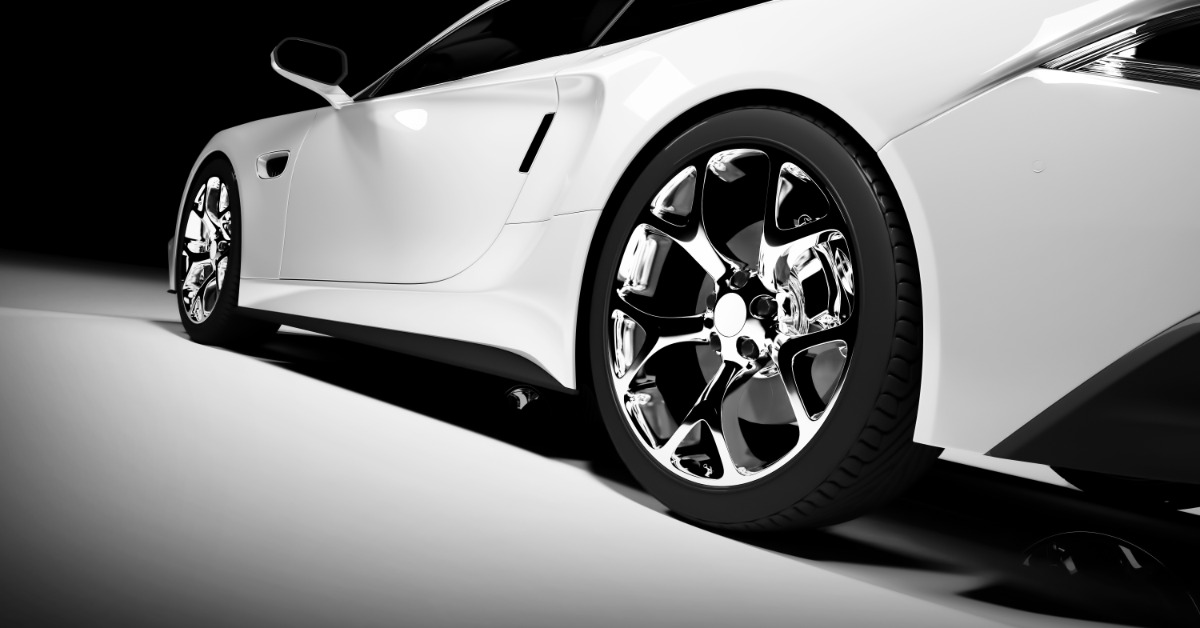 A white sports car with polished chrome wheels sits under dramatic studio lighting against a dark background.