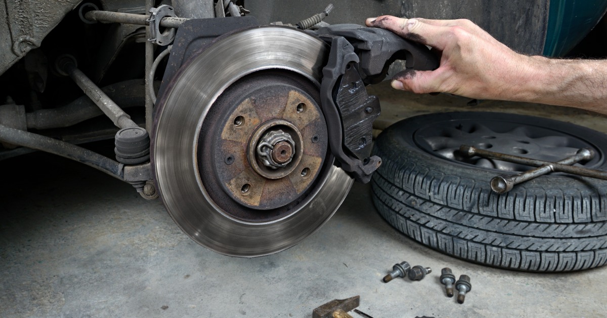 Close-up of a mechanic inspecting a worn brake rotor and brake pad on a vehicle with the wheel removed in a repair garage.