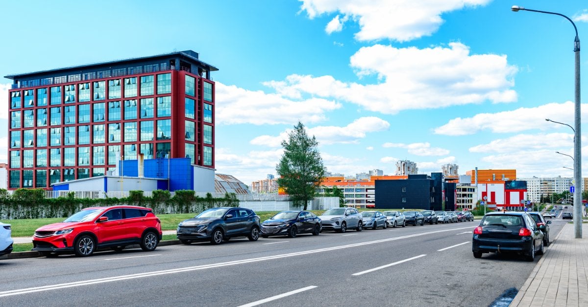 A Simple Guide to Curb Rash and How to Repair It Row of cars parked along a wide city street with a large glass office building and blue sky in the background.