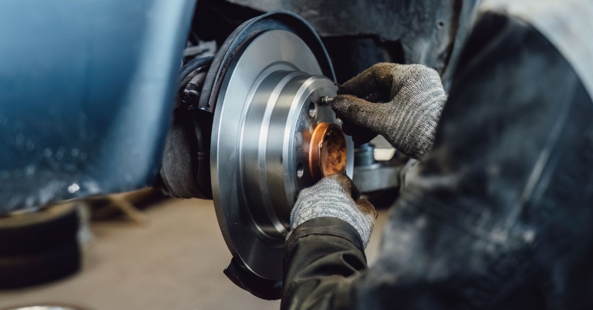 Brake Rotor Lifespan Explained: What Every Driver Needs to Know A gloved mechanic installs a brake pad onto a silver rotor during a brake service in an auto repair shop.