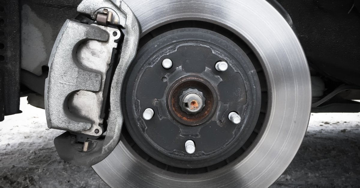 Brake Rotor Lifespan Explained: What Every Driver Needs to Know A bare vehicle wheel hub showing a silver brake rotor and gray caliper assembly with visible lug bolts.