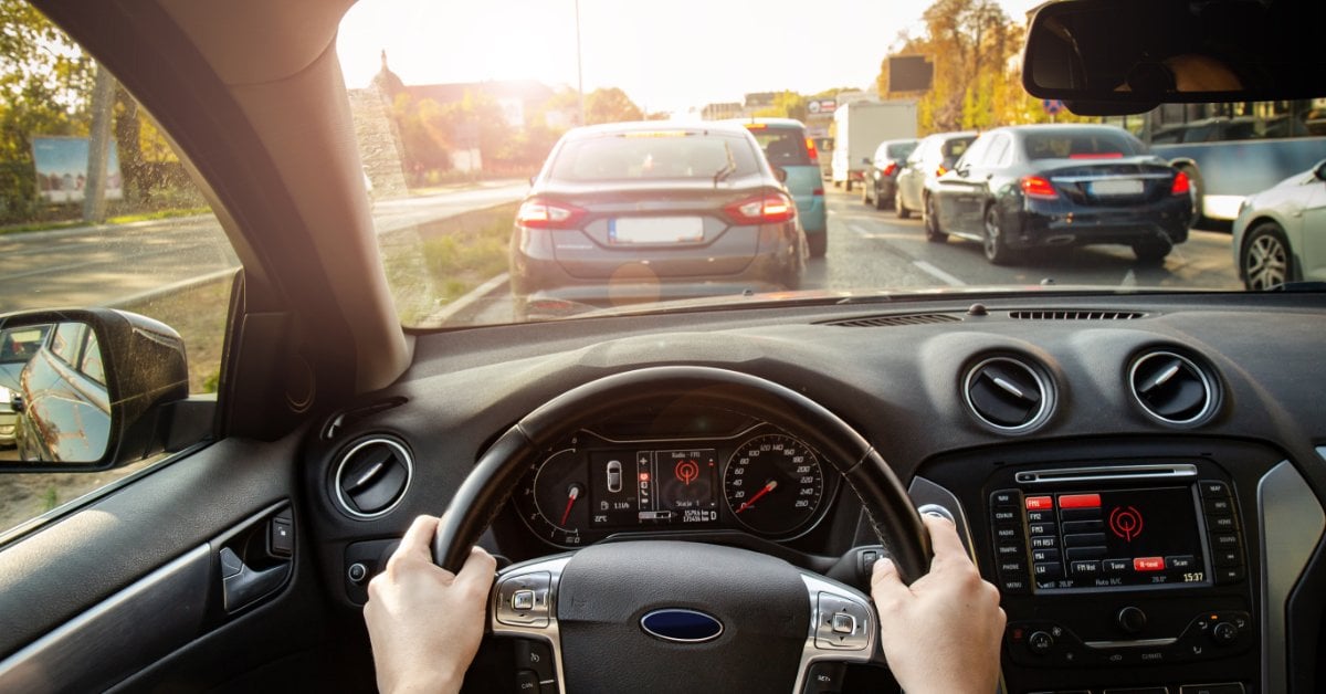 Brake Rotor Lifespan Explained: What Every Driver Needs to Know A first-person driver perspective inside a vehicle with both hands on the wheel, approaching slow city traffic at mid-afternoon.