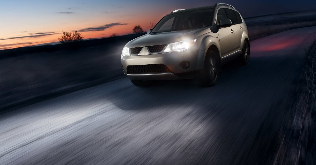 An SUV drives at dusk with bright working headlights illuminating the road, showing why headlight condition matters.
